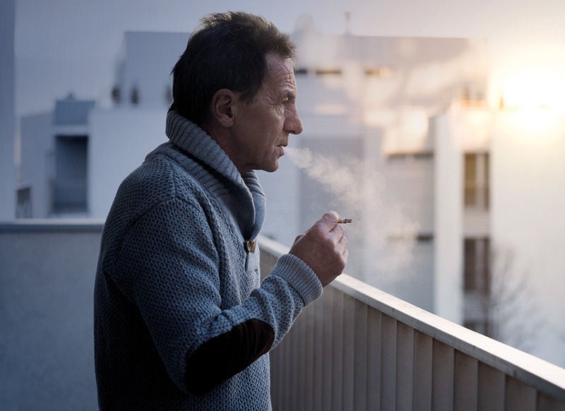 Ein Mann mit Zigarette steht rauchend auf einem Balkon
