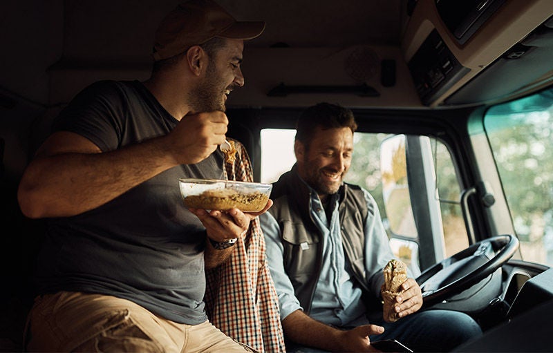 zwei Männer in einem LKW essen lächelnd