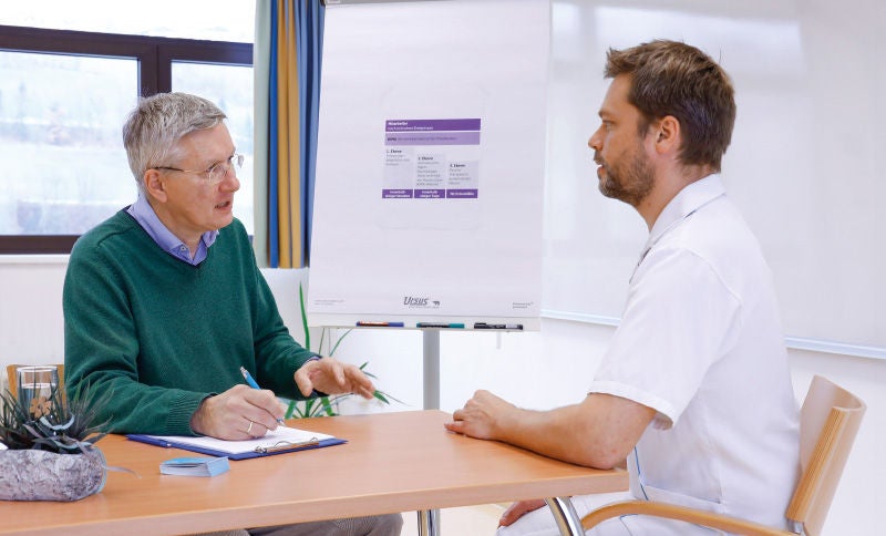 Zwei Männer sitzen einander gegenüber und führen ein Gespräch in einem Besprechungsraum.