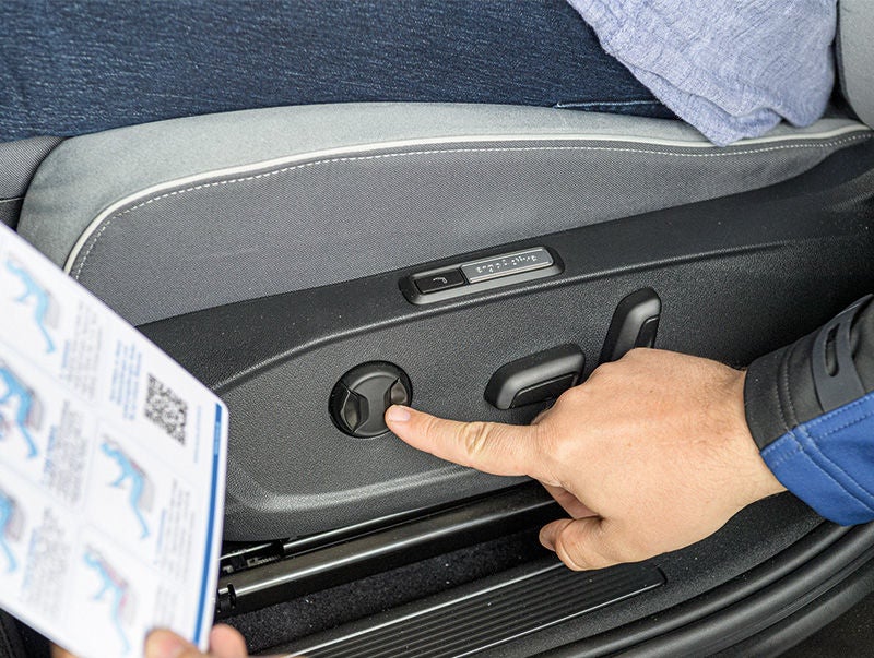ein Finger drückt auf einen Knopf an der Autotüre, die andere Hand hält eine Anleitung