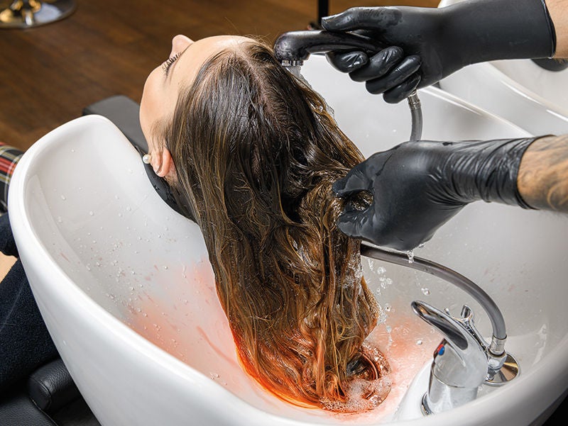 zwei Hände mit Handschuhen waschen Farbe aus dem Haar einer Frau