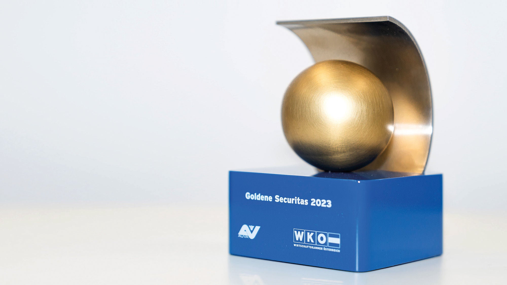 eine kleine Skulptur mit einer goldenen Kugel auf einem blauen Podest mit der Aufschrift Goldene Securitas 2023, AUVA, WKO