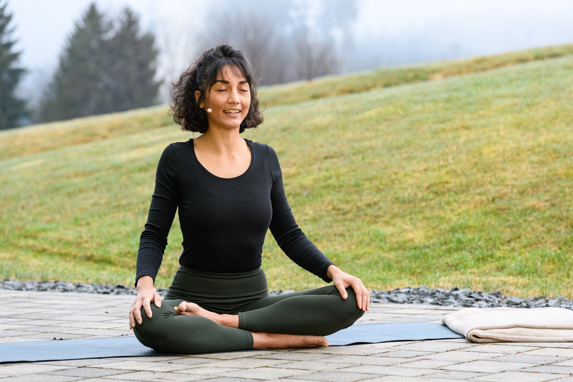 Yoga-Profi Sara Lyn Chana sitzt im Lotussitz im freien auf einer Matte