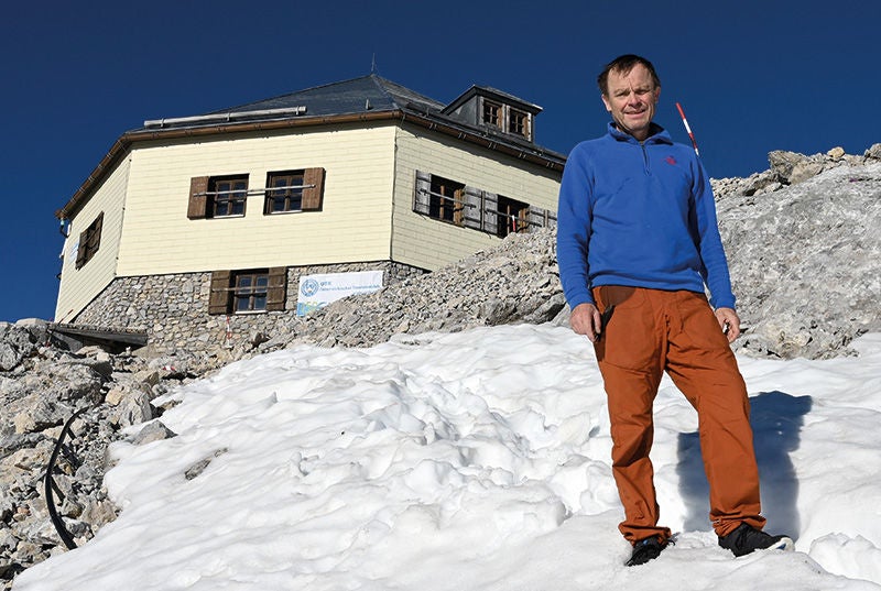 der Hüttenwirt im Schnee vor seiner Hütte