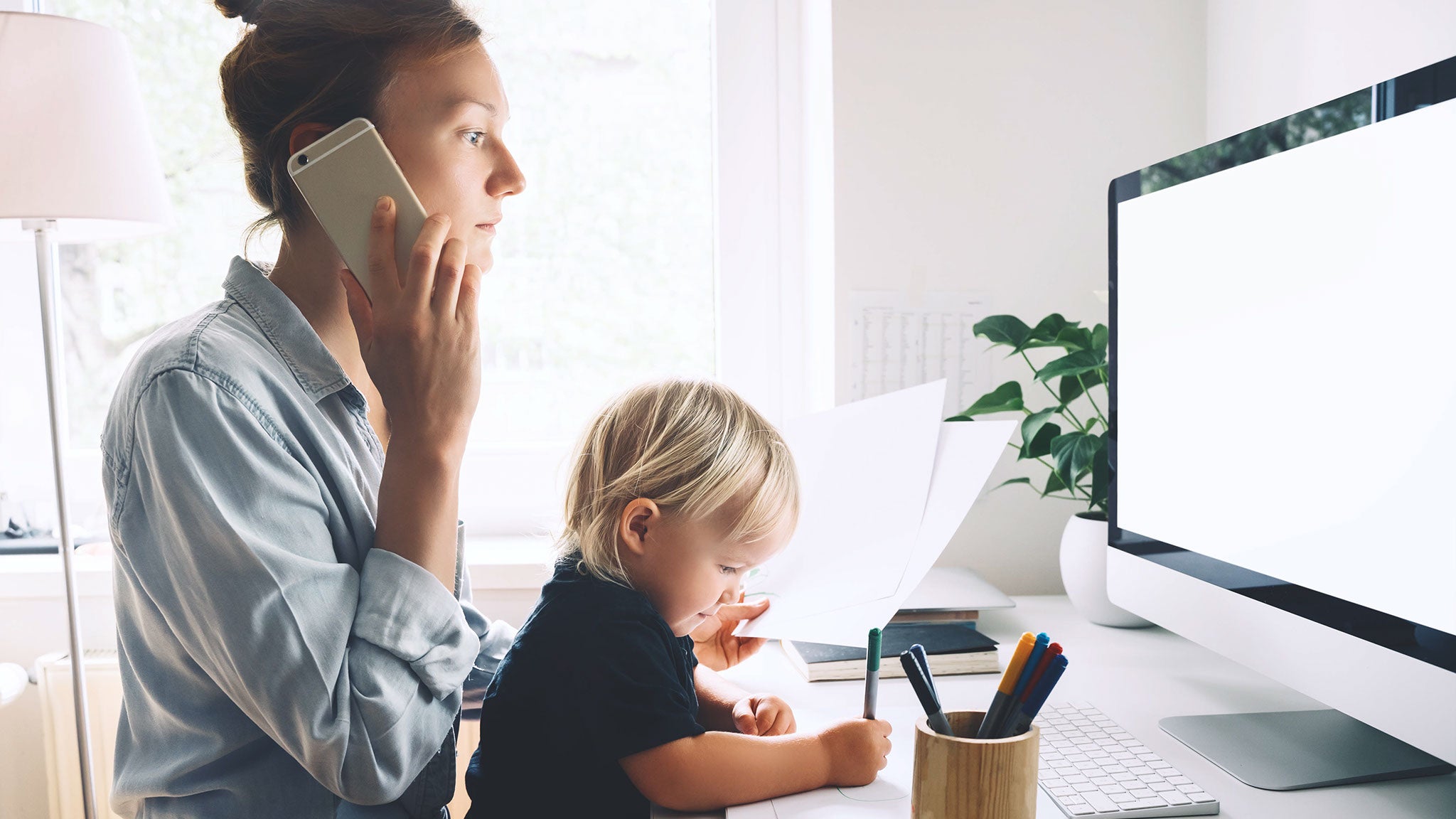 Eine Mutter sitzt telefonierend vor dem Computer und hat ihr kleines Kind auf dem Schoß