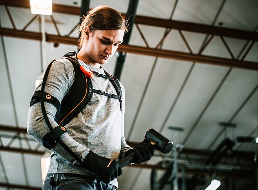 Ein Arbeiter mit einem umgeschnallten Exoskelett hält einen schweren Hammer in der Hand.