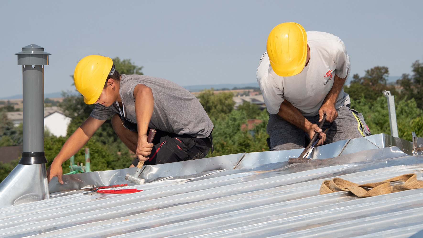 Zwei Männer mit Helm, die auf einem Aludach in der Sonne Arbeiten verrichten.