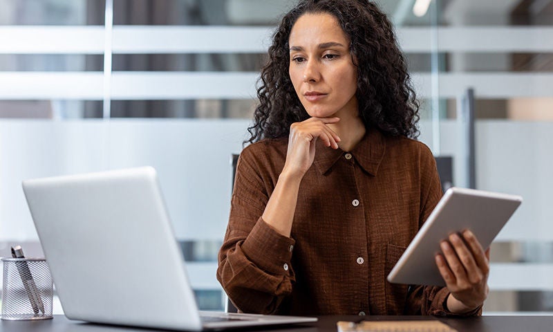 Frau arbeitet konzentriert mit Laptop und Tablet an einem Schreibtisch – symbolisiert digitale Arbeitsmittel im Büroalltag
