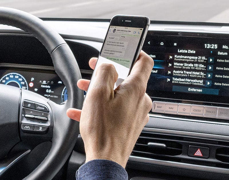eine Hand eines Autofahrers, das ein Hand bedient, dahinter ein aktives Navigationssystem