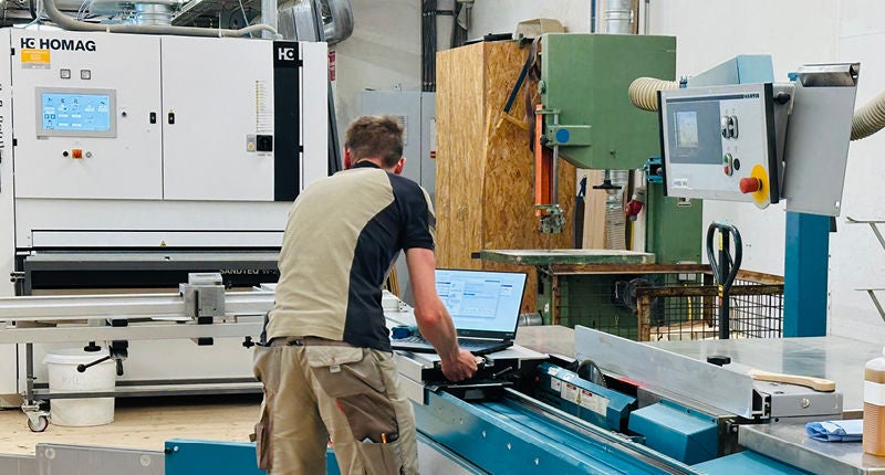 Mitarbeiter wartet mithilfe eines Laptops eine Holzbearbeitungsmaschine in einer Werkstatt.