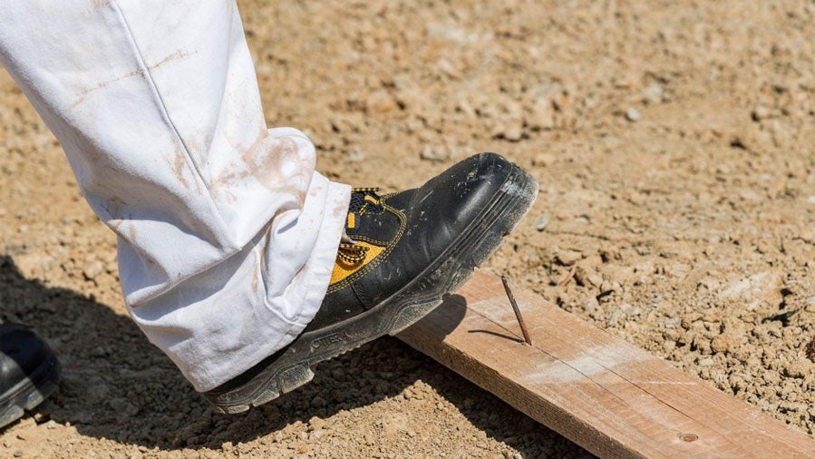Arbeiterschuh tritt auf einen Nagel