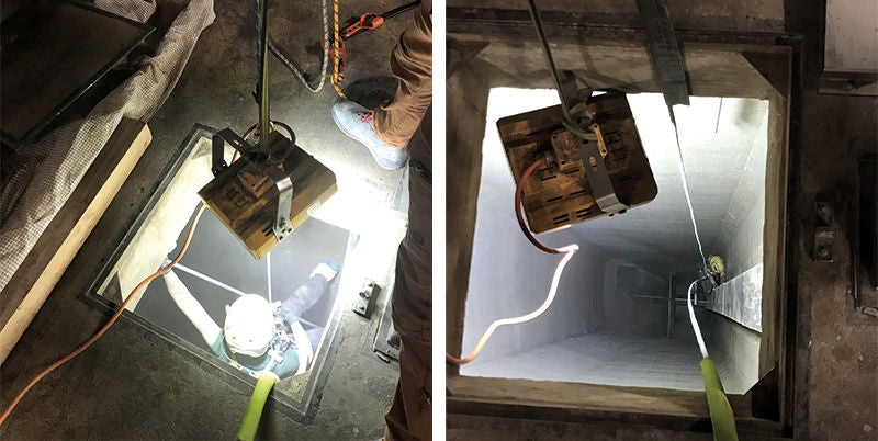 eine Person seilt sich in einen Behälter ab, darüber hängt eine Lampe um den Behälter zu erhellen; eine lamp bestrahlt den Eingang eines Behälters