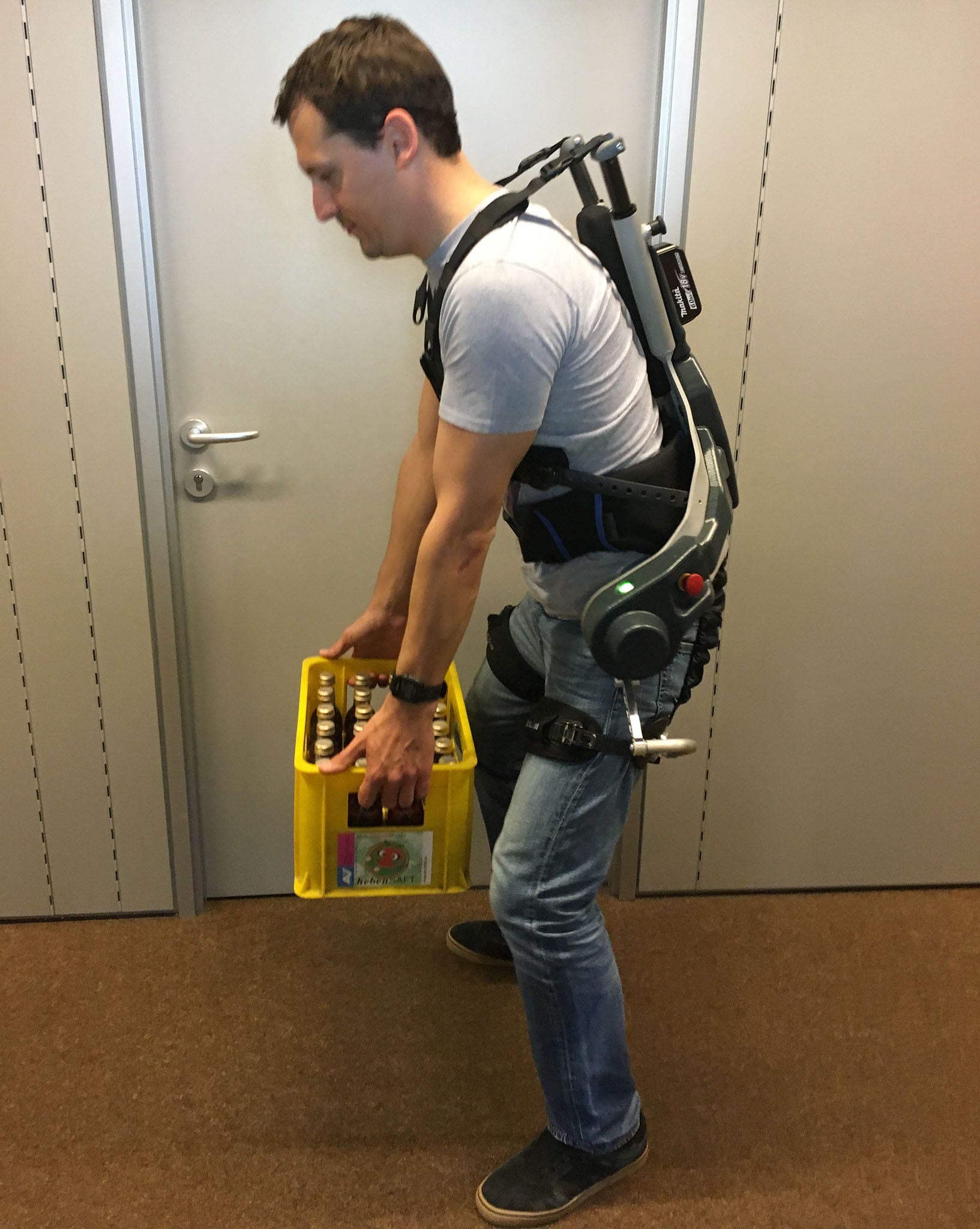 Ein Mann mit angelegtem aktivem Exoskelett hebt eine Getränkekiste