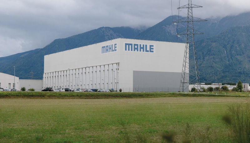 Großes Industriegebäude mit der Aufschrift „Mahle“ vor einer Bergkulisse.