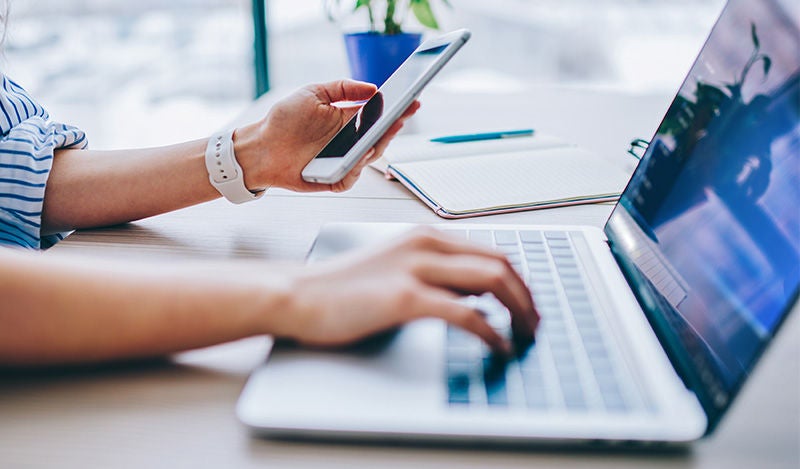 Eine Person arbeitet an Laptop und Smartphone – 
