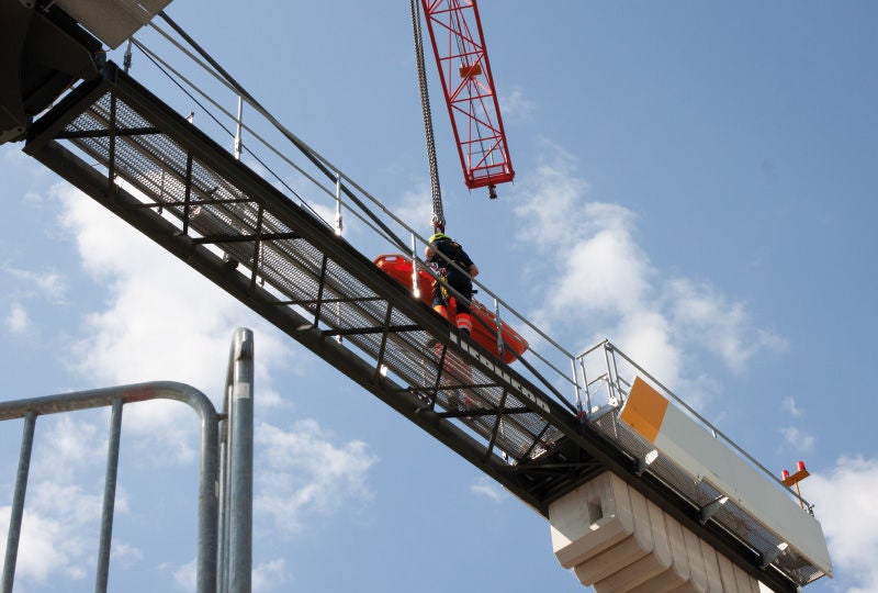 Arbeiter mit Sicherheitsausrüstung arbeitet hoch oben auf einer Brückenkonstruktion unter freiem Himmel.