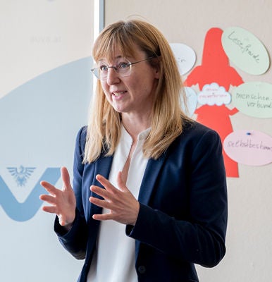 Vortragende gestikuliert vor einem mit bunten Notizzetteln beklebten Whiteboard.
