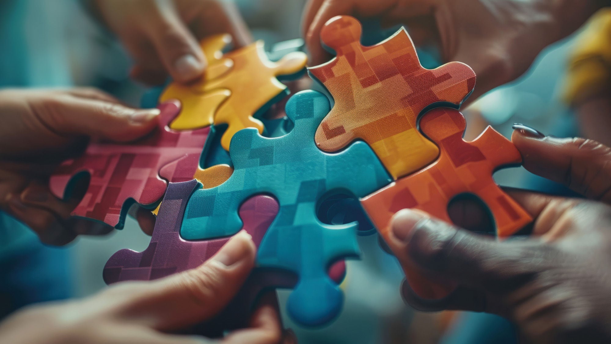 Hände mehrerer Personen halten bunte Puzzleteile, die zusammengefügt werden, als Symbol für Zusammenarbeit und Vielfalt.
