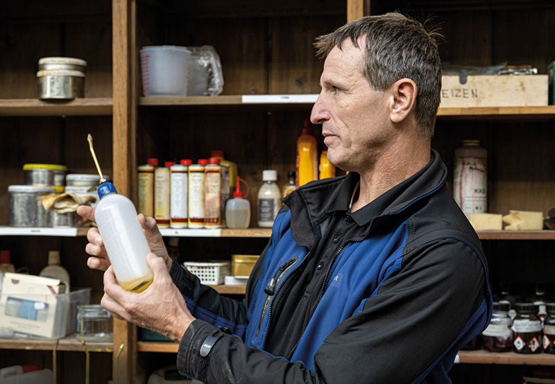 ein Mann hält eine Plastikflasche, dahinter ein Regal mit verschiedenen Gefässen