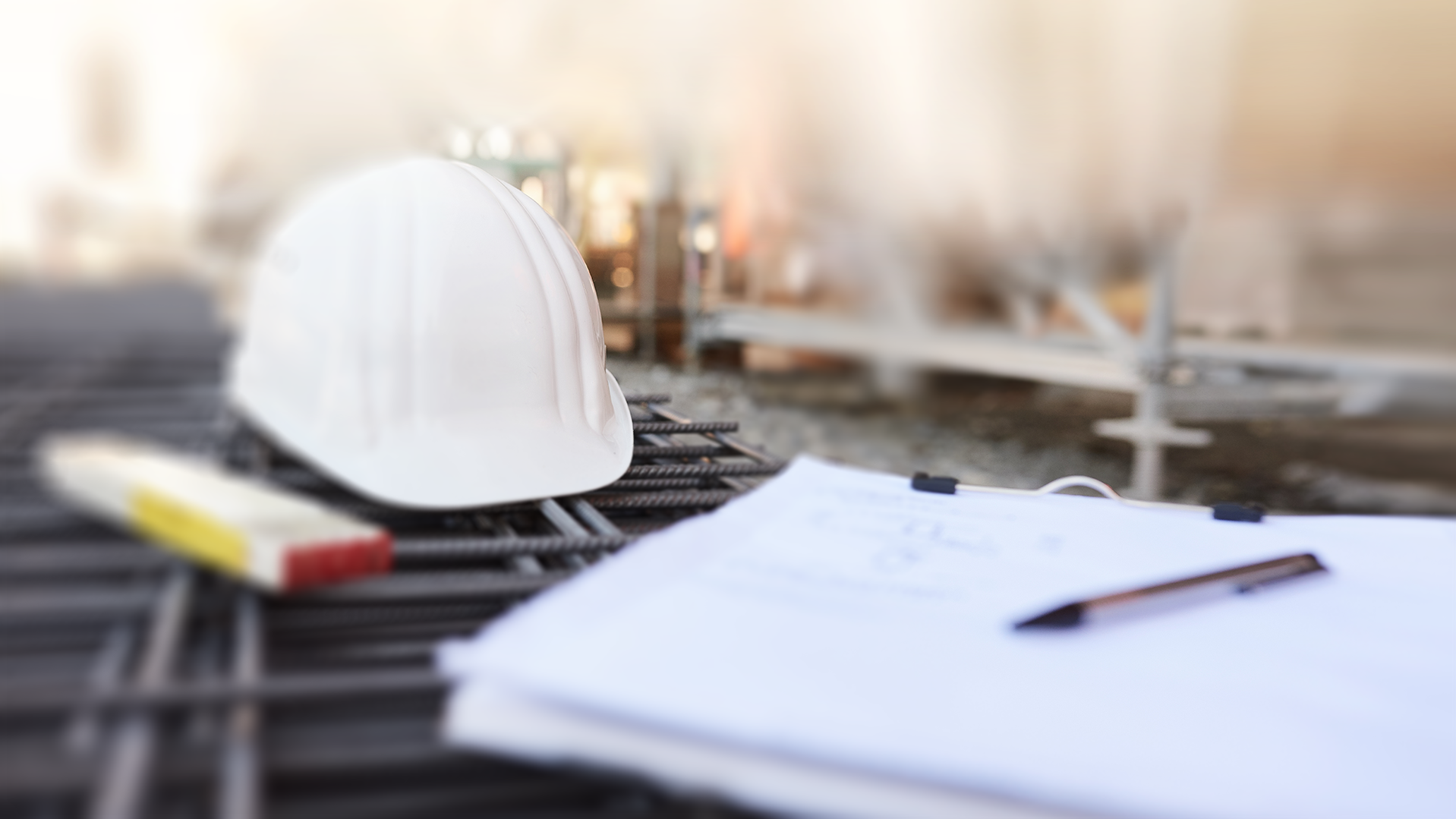 Man sieht eine Baustelle. Auf Gitterträgern liegen ein Schutzhelm, ein Maßstab und eine Schreibunterlage
