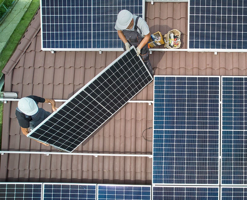 Men workers installing photovoltaic solar moduls on roof of house. Engineers in helmet building solar panel system outdoors. Concept of alternative and renewable energy. Aerial view.