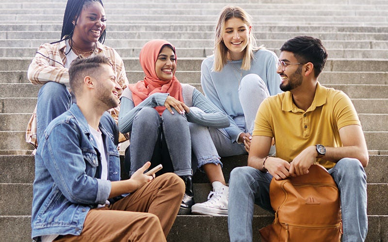 Junge Menschen verschiedenster Herkunft sitzen in fröhlicher Stimmung auf einer Stiege beisammen