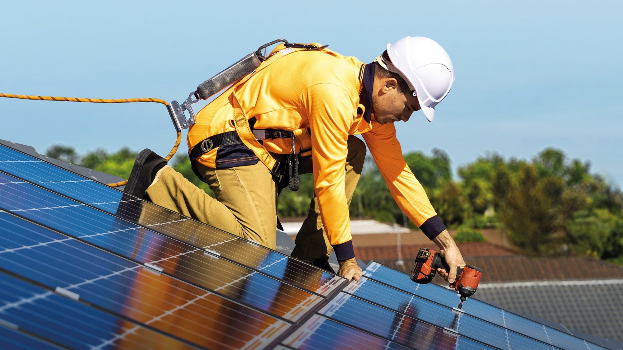 ein gut gesicherter Bauarbeiter mit Helm und Schutzausrüstung montiert Photovoltaikpanels auf einem Dach