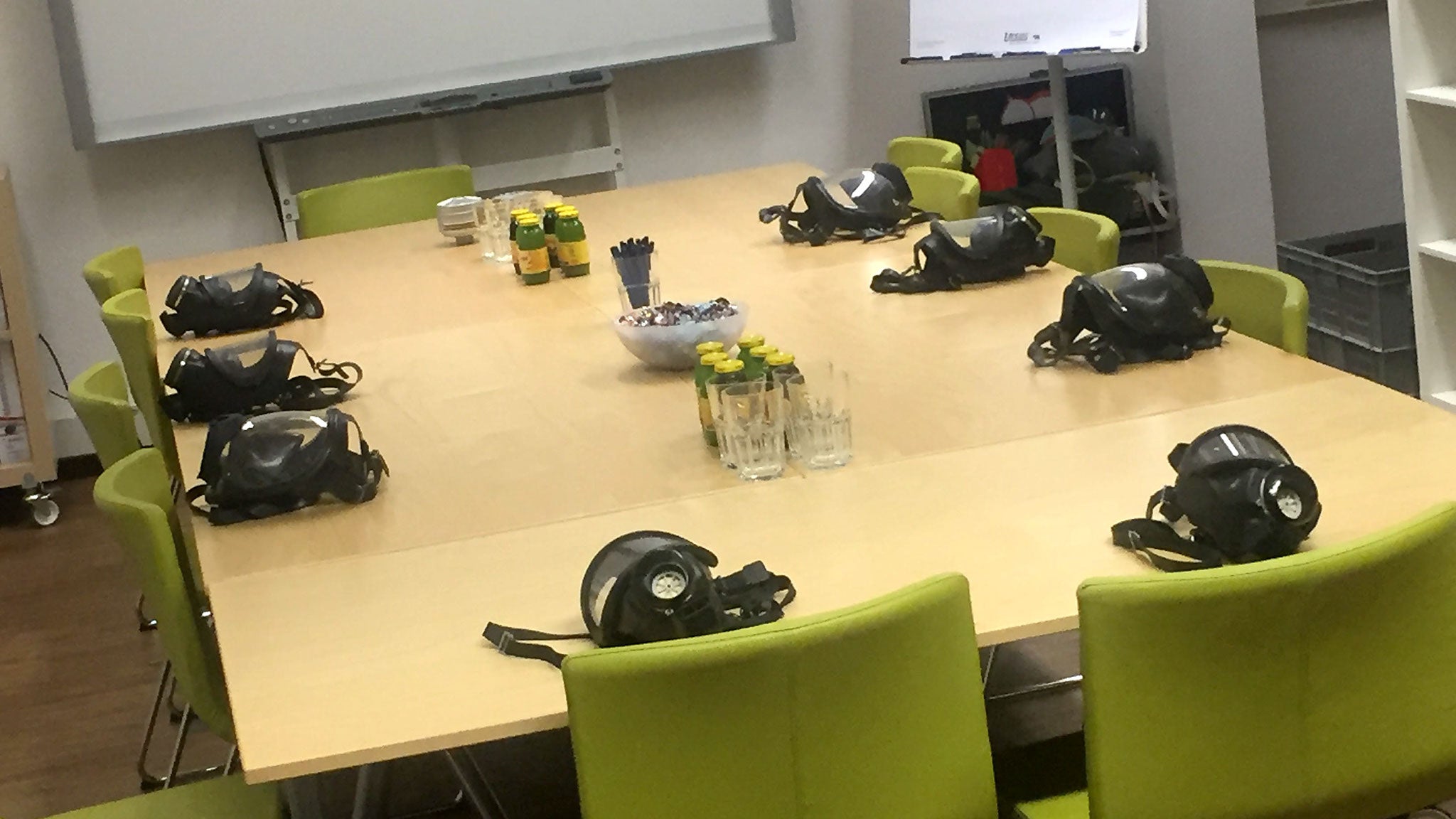 Schulungsraum mit Tisch, Flipchart etc. Am Tisch liegen Schutzmasken mit Schutzbrille