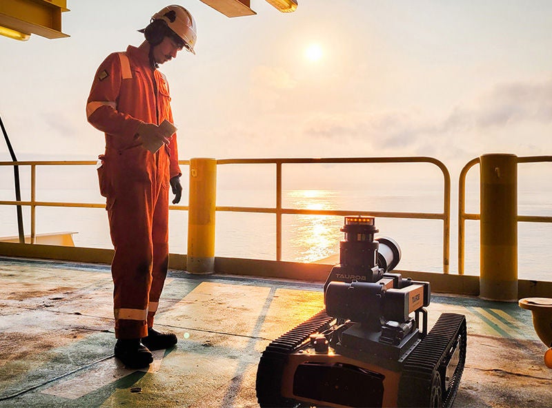 Techniker in Schutzausrüstung beobachtet einen Inspektionsroboter auf einer Offshore-Plattform