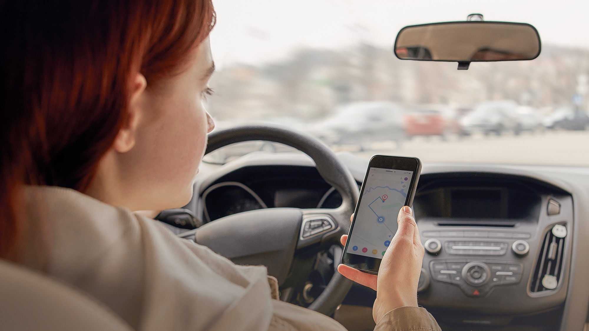 jugendliche Autofahrerin hält ihr Smartphone mit der Navigation in der Hand