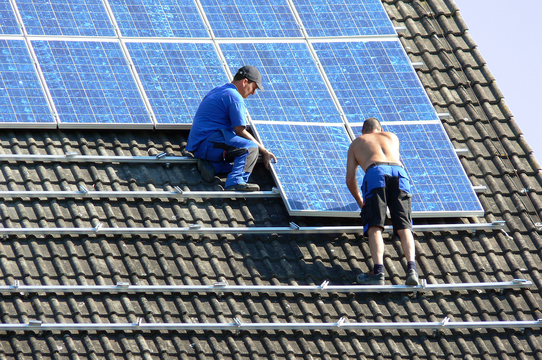 Ein Mann mit nacktem Oberkörper arbeitet auf einem Dach mit einem Photovoltaik Panel