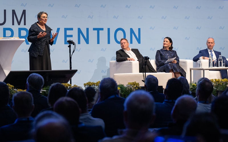 Eröffnung des Forums Prävention 2026 in Innsbruck mit Keynote-Speakerin Elisabeth Oberzaucher am Stehpult und drei weiteren Personen auf der Bühne.