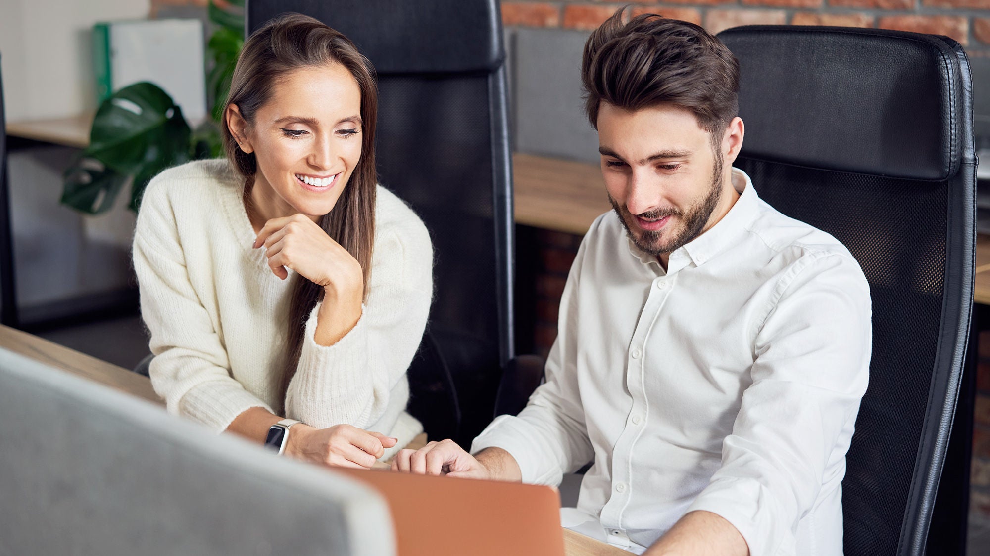 eine Frau und ein Mann sitzen lächelnd nebeneinander und blicken in einen Computer