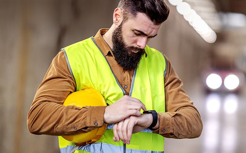 Bauarbeiter mit Warnweste blickt auf seine Smartwatch – symbolisiert Wearables als neue Arbeitsmittel