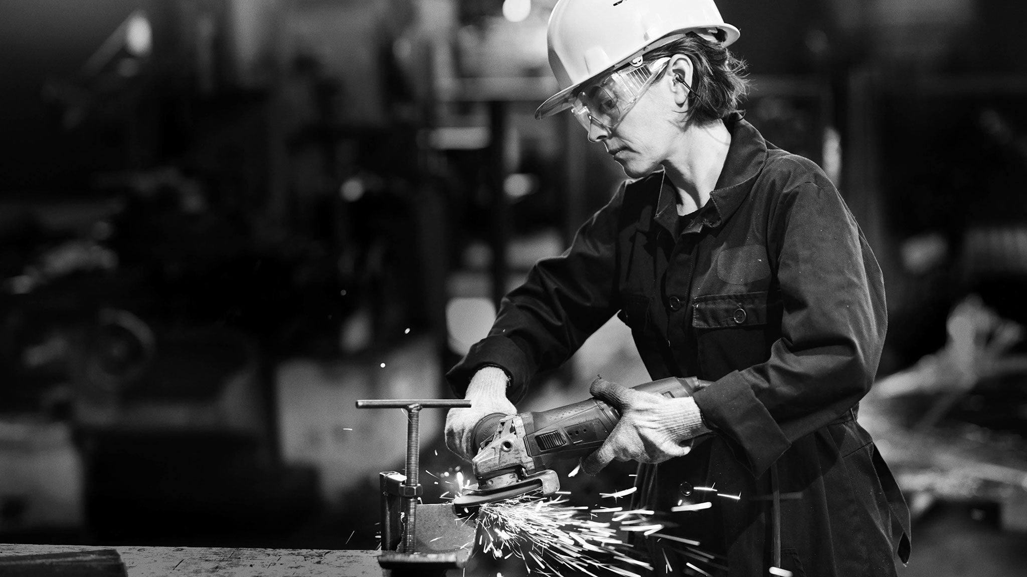 Das Bild zeigt eine Arbeiterin mit Helm, Schutzbrille und Gehörschutz in einer Produktionsanlage