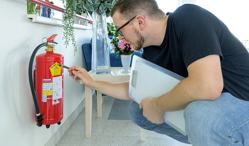 ein Mann begutachtet die Plakette eines Feuerlöschers