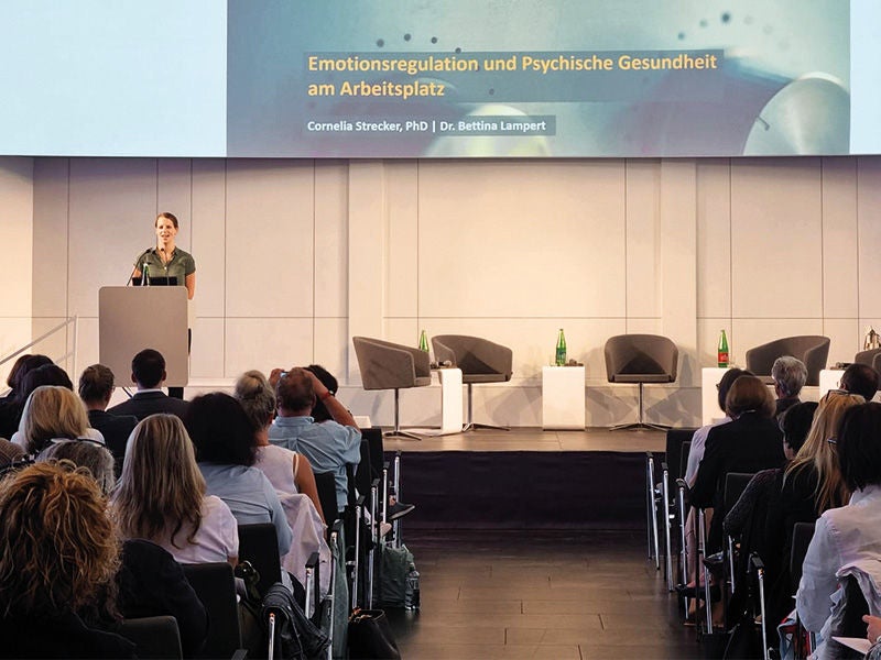 in einem Saal sitzen versammelt zahlreiche Menschen und folgen einem Vortrag