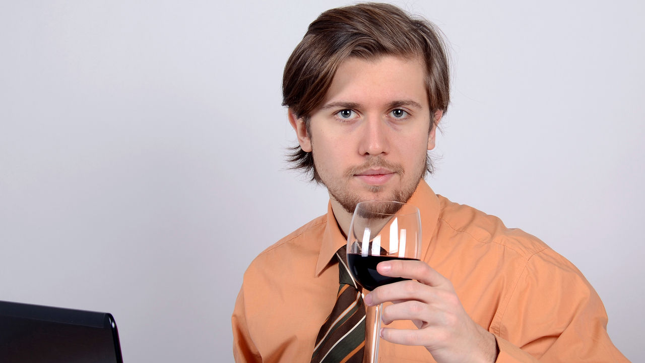 Junger Mann mit Krawatte trinkt am Arbeitsplatz ein Glas Wein.
